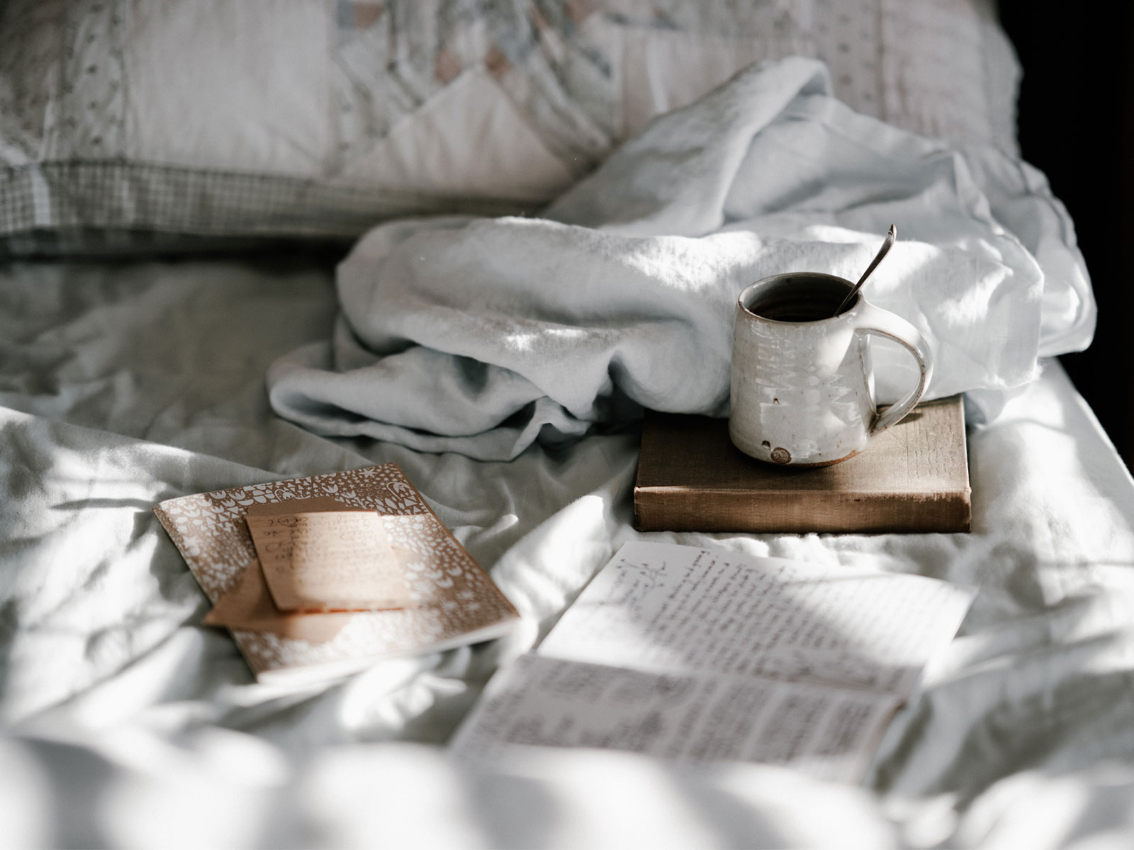 Linen sheets on a bed with a ceramic coffee mug in the sun